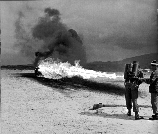 LeslieAnn dressed as boy, demonstrates flame-thrower at Ford Ord, 1962.