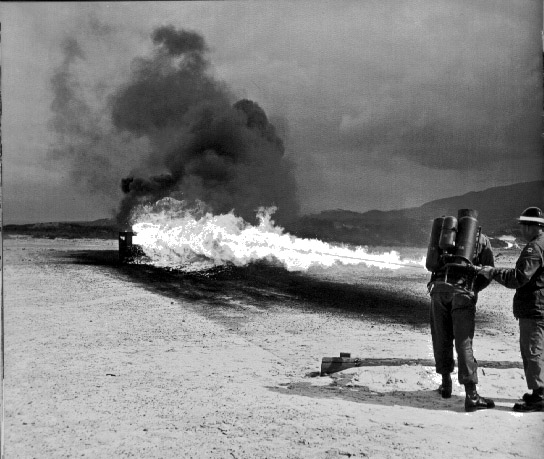 LeslieAnn dressed as boy, demonstrates flame-thrower at Ford Ord, 1962.